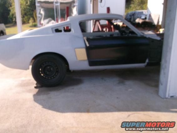 Side view of a 1967 Ford Mustang fastback in primer with doors open, undergoing restoration
