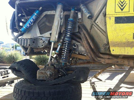 Off-road buggy's front suspension with multiple King shocks and a completely flat tire resting on another tire