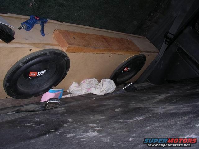 Interior view of a vehicle with a large wooden subwoofer box holding two JBL speakers