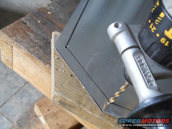 Drill bit making a hole in a metal sheet on a wooden workbench