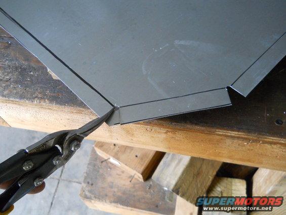 Sheet metal being cut with tin snips on a wooden workbench