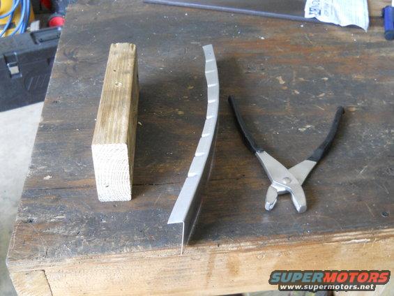Wood block, curved metal trim piece, and pliers on a workbench