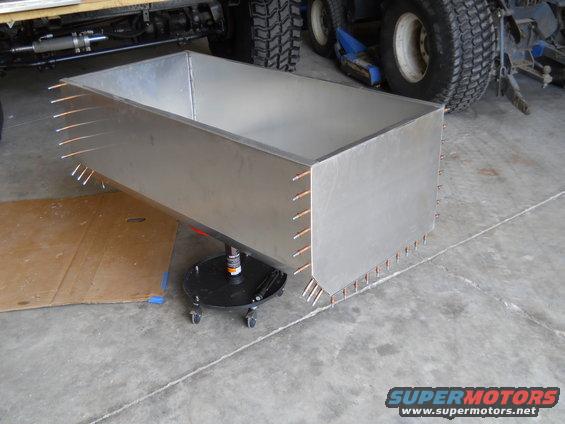 Custom metal box on a stand, with vehicle parts and tires in the background