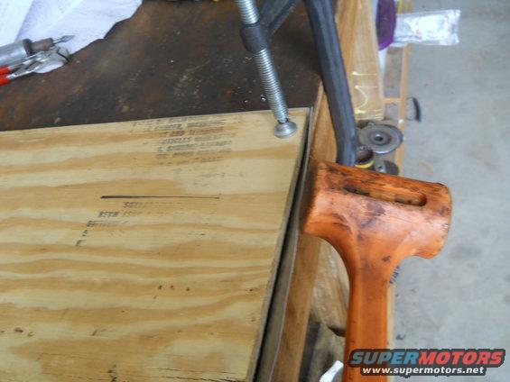 Workbench with a clamp holding plywood and a rubber mallet nearby. Text is visible on the plywood