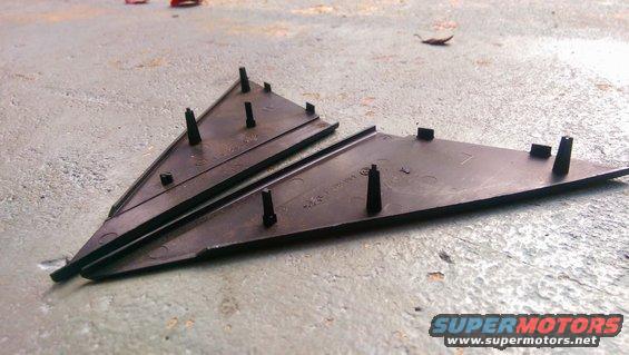 Two black plastic trim pieces with mounting posts on a concrete surface