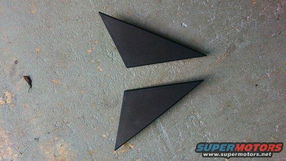 Two black triangular trim pieces, possibly for car mirrors, on a concrete surface