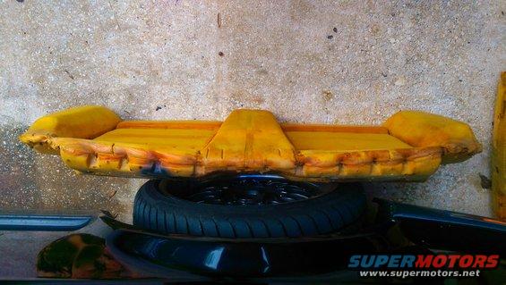 Yellow foam car seat cushion with visible wear, resting on a tire and car parts