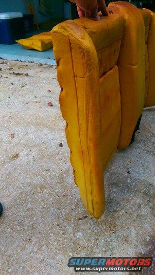 Yellow foam from a car seat is on the ground. A hand is touching the top