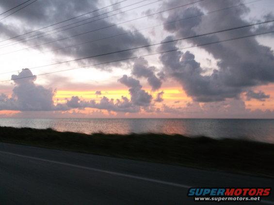 Ocean sunset with clouds and power lines over a road