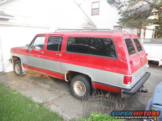 1990 Chevrolet Suburban parked outside a garage, side view. Red and silver paint