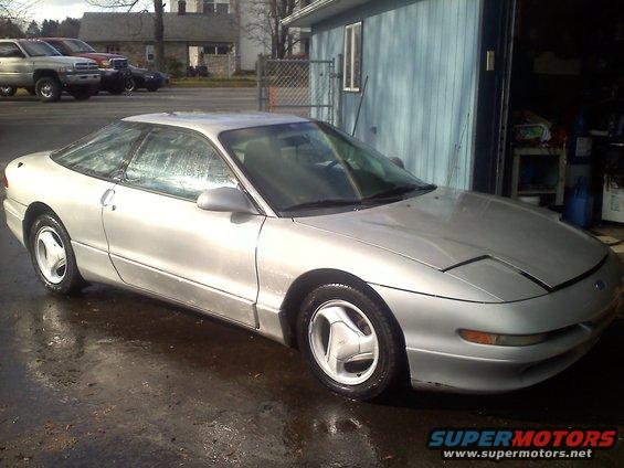 Silver 1993 Ford Probe GT parked on wet asphalt in front of a blue garage