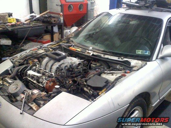 Silver car's engine compartment open, showing V6 engine and various parts
