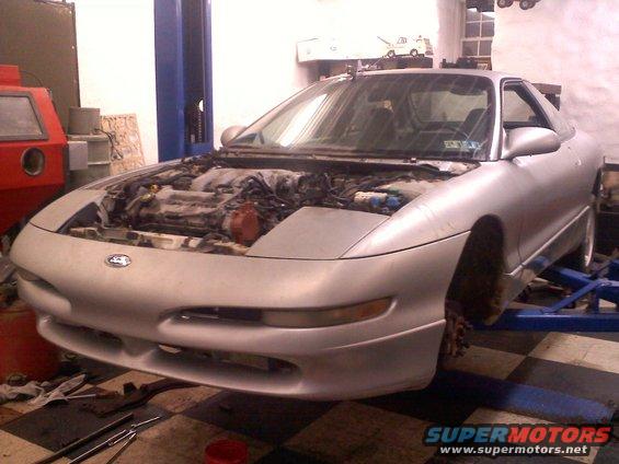 Silver 1993 Ford Probe GT on a lift with the hood open, showing the engine bay. The front end is visible