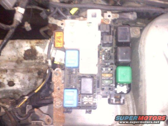 Engine bay fuse box with blue, black, and green relays, and a watermark for Supermotors.net