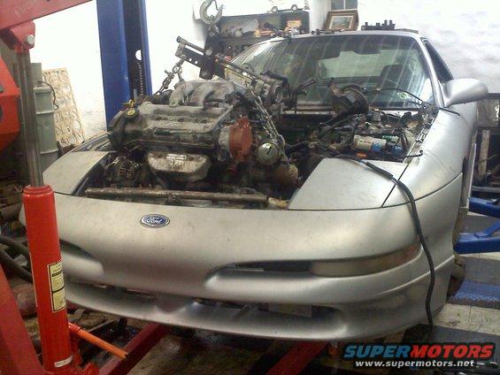 Silver Ford Probe in a garage with its engine being lifted out by a hoist