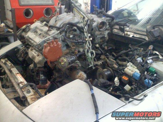 Engine being lifted out of a car's engine bay, showing complex wiring and mechanical parts