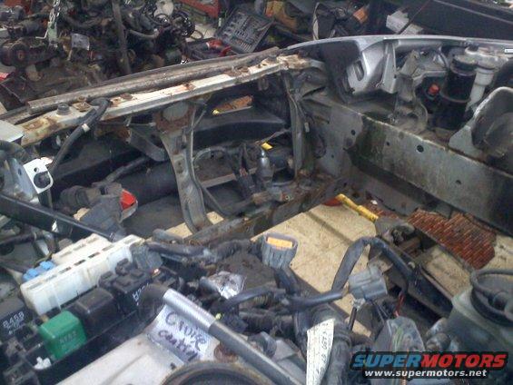 Car engine bay with parts removed, showing wiring and frame. Some labels are visible