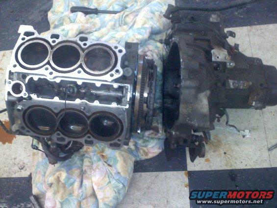 Engine block with six cylinders and attached transmission, resting on a patterned cloth