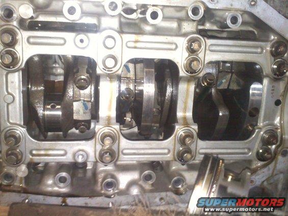 Engine block with crankshaft and connecting rods visible, some oil residue present. A piston is partially visible on the right