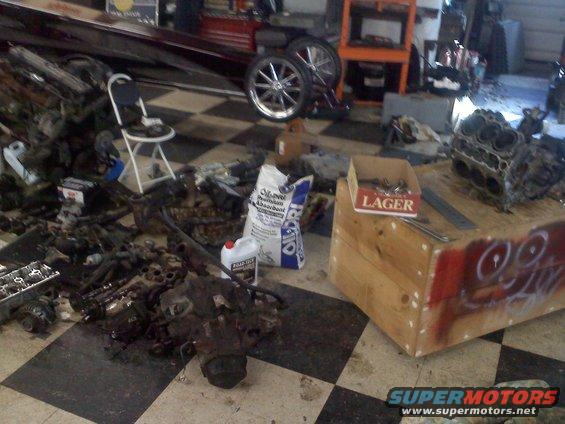 Engine parts are scattered on a checkered floor next to a boat hull and some tires