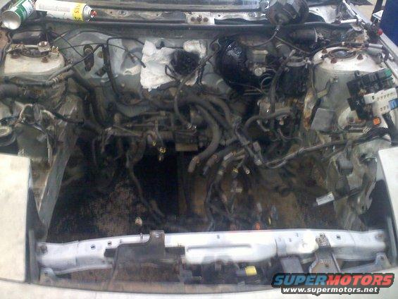 Engine bay with wiring and hoses disconnected, car disassembled