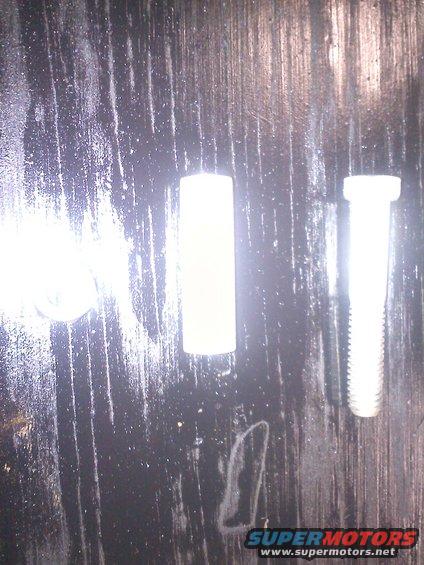 two bolts and a white cylindrical part on a dark, textured surface