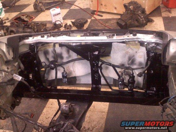 Car engine bay with parts removed for repair, showing wiring and frame