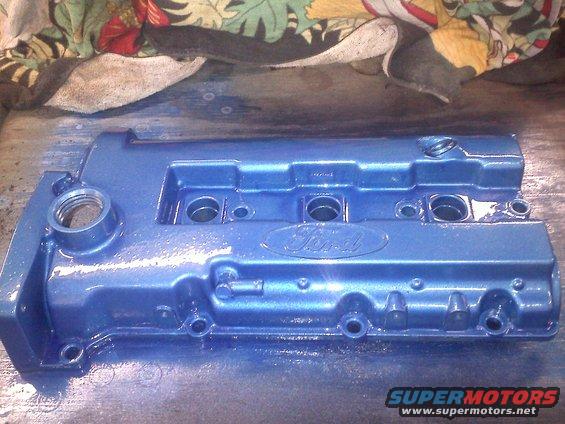 Blue Ford valve cover with embossed Ford logo, showing bolt holes and threaded openings