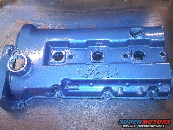 Blue metallic Ford valve cover with embossed Ford logo and threaded openings