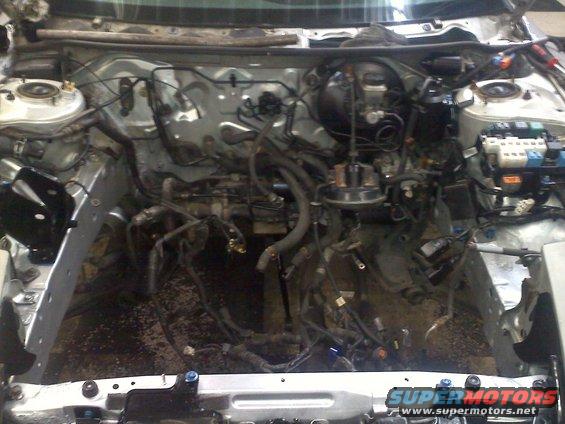 Empty engine bay showing wiring harnesses, brake booster, and suspension components