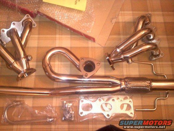 exhaust headers, pipes, gaskets, and bolts laid out on a checkered surface