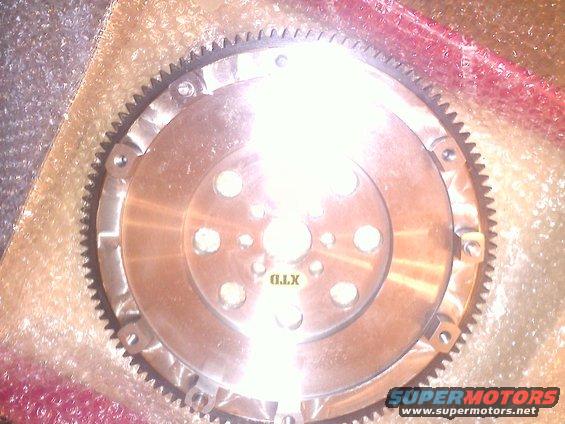 Metal flywheel with gear teeth and bolt holes, some text visible