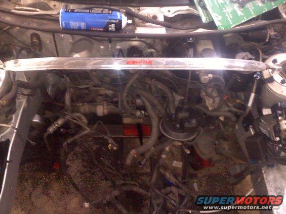 Engine bay with a chrome strut bar across the top. A blue can is on the left