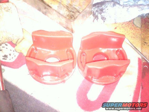 Two red suspension bushings on a patterned cloth with a "Supermotors.net" watermark