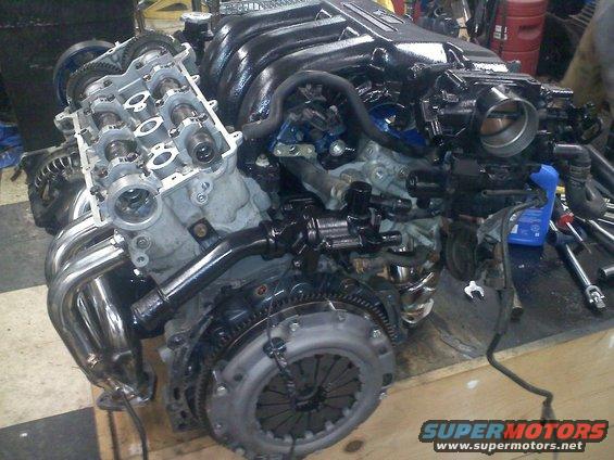 Engine with shiny exhaust headers and black intake manifold, clutch visible