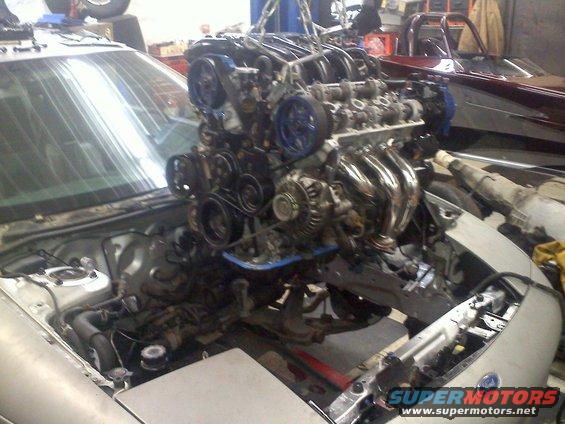 Engine is being lifted out of a car in a garage. Another car is visible in the background