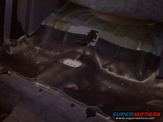 Car interior floor showing pedals and dark carpeting. A watermark reads SUPERMOTORS.NET