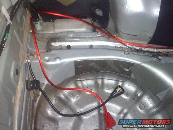 Car trunk interior showing red and black wiring, spare tire well, and metal body panels