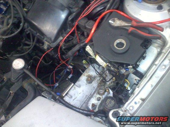 close-up of car engine bay with wires, fuse box, and tools