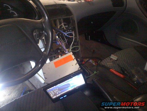 Car interior showing dashboard with wires exposed and a new stereo being installed