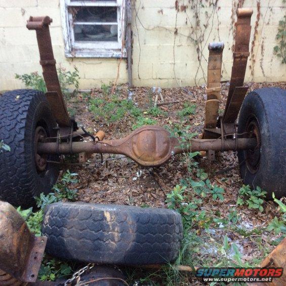 rear axle assembly with leaf springs and tires, sitting outside near a building