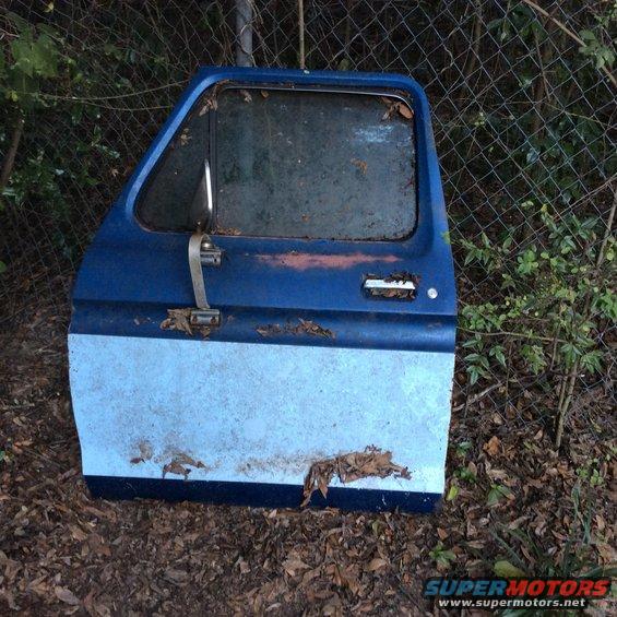 Blue and light blue two-tone Ford truck door, rusted and weathered, lying on the ground