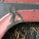 1979 Ford Bronco - Close-up of a red metal part with significant rust and peeling paint, revealing a triangular area of bare metal underneath.