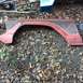 1979 Ford Bronco - A red fender with a dark stripe is shown on the ground, surrounded by leaves and dirt.