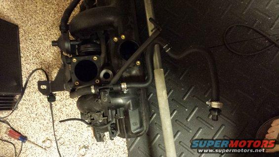 Engine intake manifold with hoses attached, lying on a textured surface