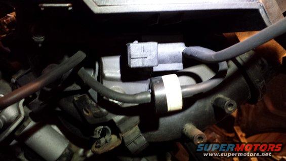 Close-up of an engine component with hoses and an electrical connector