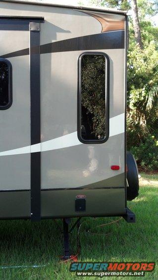 Travel trailer side with dark green and grey paint, a vertical window, and a spare tire mounted on the back