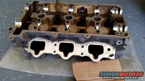 Engine cylinder head with intake ports visible. Cardboard with text and Supermotors logo