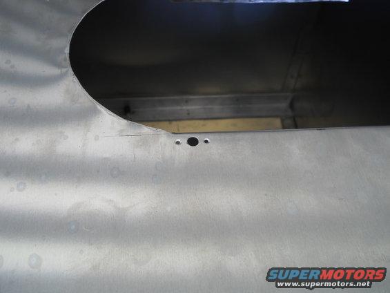 Unpainted metal panel with a large cutout and two small holes, showing some dents and scratches