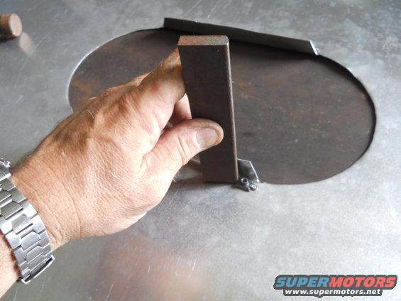 Hand holding metal bracket over circular cutout on metal surface